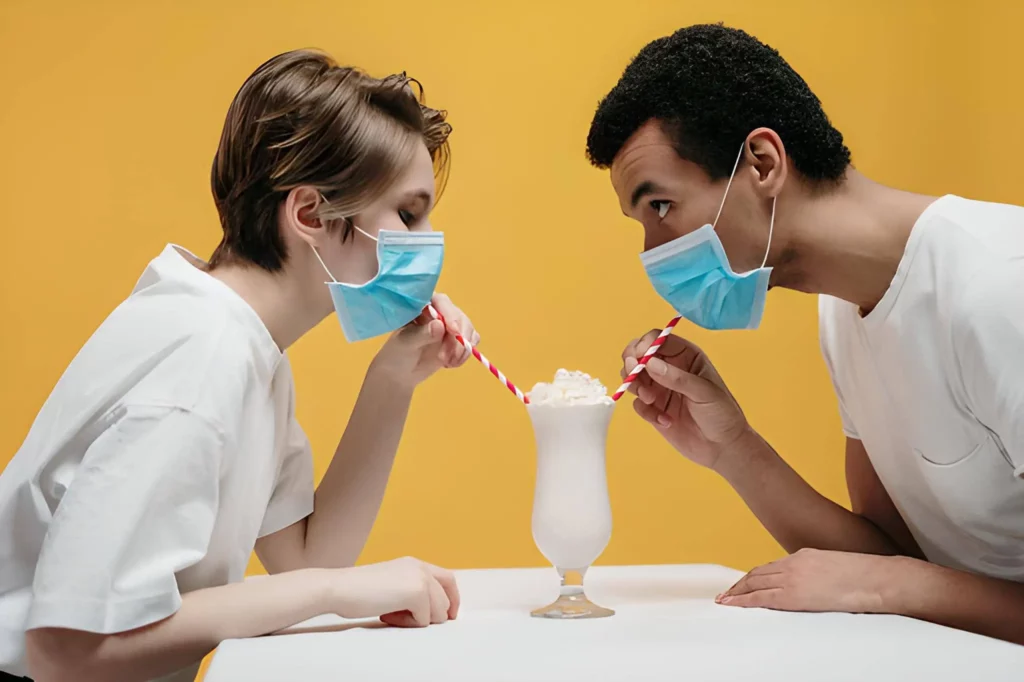 A couple in masks drink a milkshake from the same cup